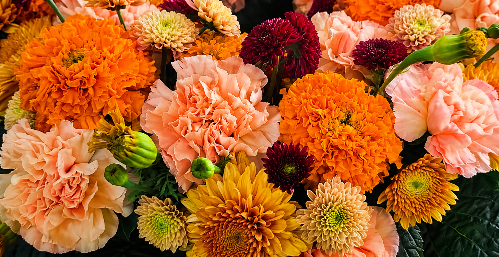 Lush blomsterarrangemang med orange tagetes, persika nejlikor och burgunder krysantemum
